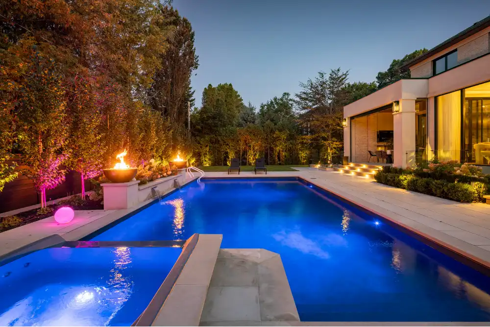 Inground pool with illuminated patio at dusk
